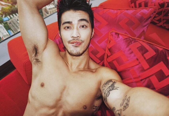 Gay man at W Shanghai - The Bund, top gay hotel. Shirtless man with tattoos, lying on red pillows. Gay travel in Shanghai, China.