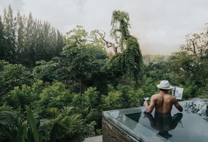 Gay man in luxury pool villa at InterContinental Khao Yai Resort, Thailand. National Park view, cocktail, hat, magazine. Relaxing gay travel.