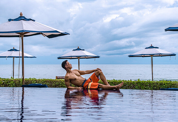 Gay man relaxing at Vana Belle, a Luxury Collection Resort, Koh Samui. Beachfront hotel in Thailand with pool and umbrellas.