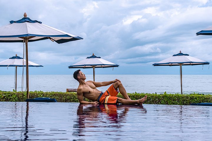 Gay man relaxing at Vana Belle, a Luxury Collection Resort, Koh Samui. Beachfront hotel in Thailand with pool and umbrellas.