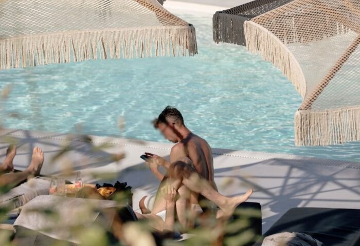 Akkadian Gay Hotel Mykonos pool scene. Two men lounge poolside at the number one gay-only hotel. Luxury travel for gay men in Mykonos.
