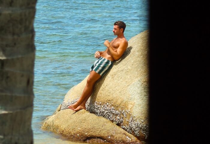 Gay man relaxing on rocks at Rocky's Boutique Resort, Koh Samui. Private beach resort, Thailand vacation. Veranda Collection Samui.