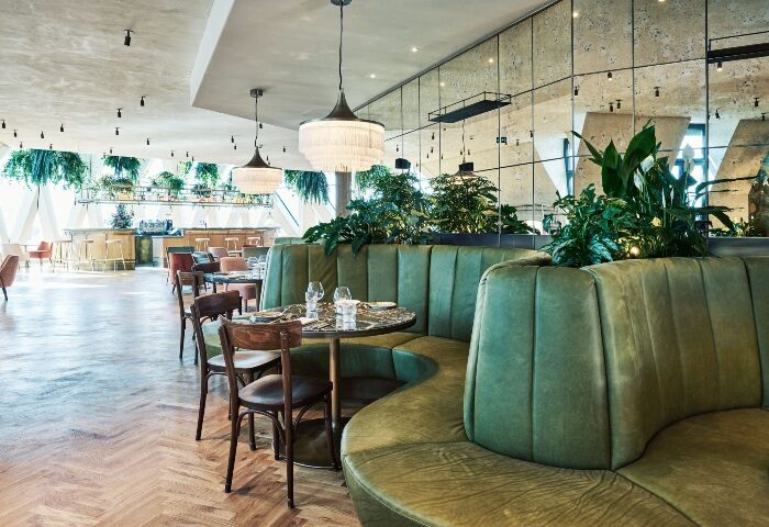Hotel MOTTO Vienna's breakfast area near gay bars: Green booth seating, tables set for dining, bar area in background. Stylish, modern design.