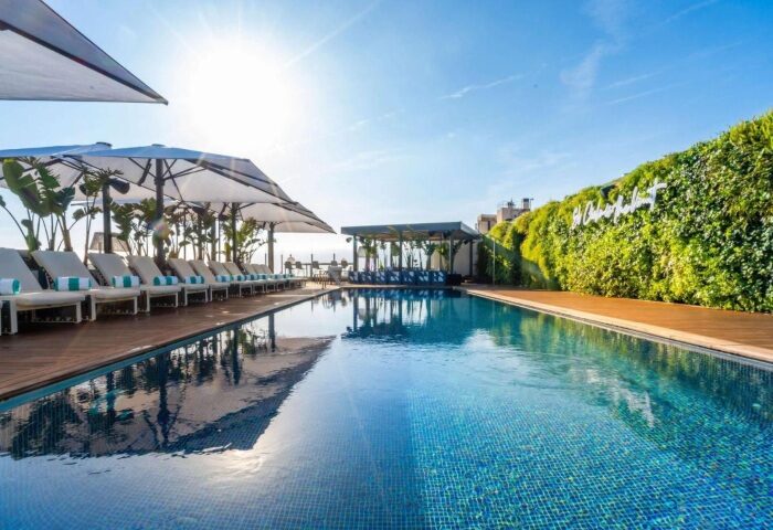 Sofitel Barcelona Skipper rooftop pool. Luxury gay hotel in Barcelona with sunbeds, umbrellas, and a green wall. Perfect for gay travel.