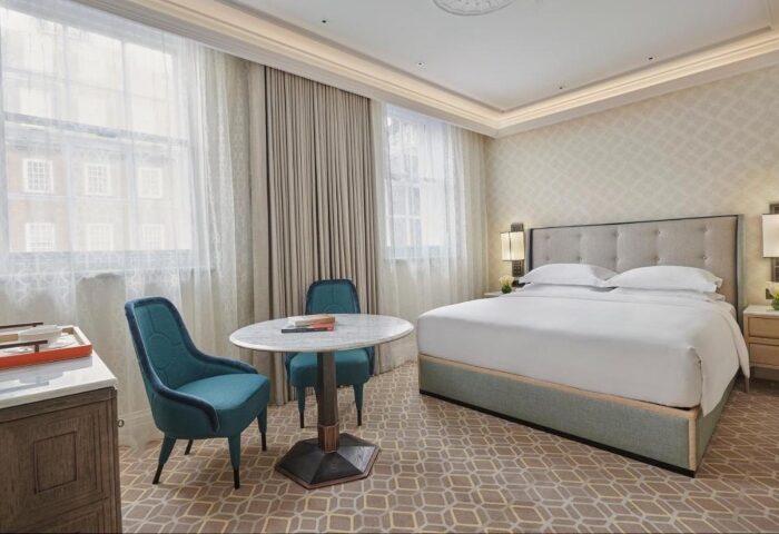 Great Scotland Yard Hotel's luxury room for gay travelers in London. Features a king bed, round table, teal chairs, and elegant decor.