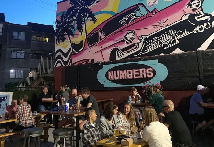 Outdoor seating at Numbers Cabaret in Vancouver. Mural with pink car and palm tree. Gay men travel advice.