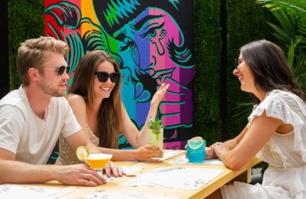 Vancouver's Numbers Cabaret: Friends enjoy cocktails at an outdoor table with a colorful mural. A gay-friendly travel destination.