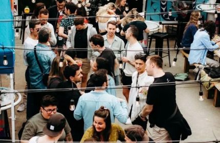 Vancouver's Numbers Cabaret crowd. A lively outdoor scene with diverse people, drinks, and string lights. Gay travel advice, nightlife.