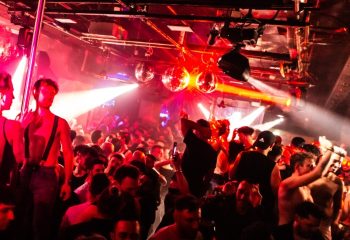 ONEWAY Discoclub Milan: Gay men dancing at a crowded party with disco balls and red lighting. Gay travel advice.