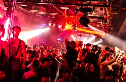 ONEWAY Discoclub Milan: Gay men dancing at a crowded party with disco balls and red lighting. Gay travel advice.