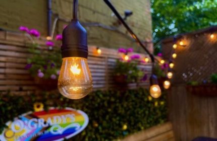 O'Grady's On Church bar in Toronto, a gay-friendly travel destination. String lights illuminate the outdoor patio, with flowers and greenery.