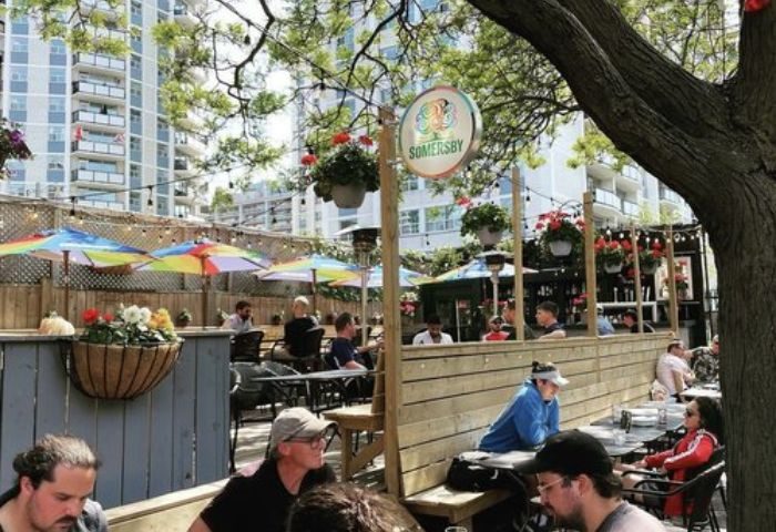 O'Grady's on Church Bar in Toronto patio. Gay bar scene with men at tables under colorful umbrellas. Somersby sign is visible.