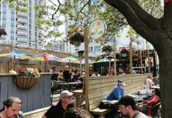 O'Grady's on Church Bar in Toronto patio. Gay bar scene with men at tables under colorful umbrellas. Somersby sign is visible.