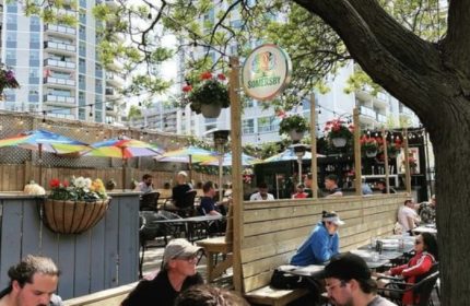 O'Grady's on Church Bar in Toronto patio. Gay bar scene with men at tables under colorful umbrellas. Somersby sign is visible.