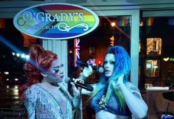 Drag queens perform at O'Grady's On Church bar in Toronto, a popular gay bar. Rainbow flag and Union Jack visible. Gay travel advice.