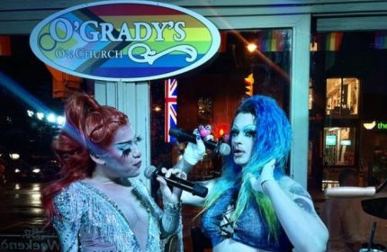 Drag queens perform at O'Grady's On Church bar in Toronto, a popular gay bar. Rainbow flag and Union Jack visible. Gay travel advice.