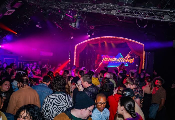 Oasis drag cabaret in San Francisco. A crowd of people at a drag show in a nightclub with a stage and pink and purple lighting. Gay travel.