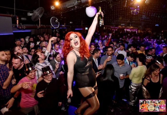 Oasis Drag Cabaret in San Francisco: A drag queen in lingerie and fishnets holds a bottle aloft in a crowded nightclub. Gay travel.