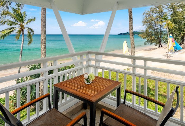 SAii Laguna Phuket ocean-front suite balcony view. Table and chairs overlook the beach. Perfect for gay travel, relaxation, and enjoying Phuket's beauty.