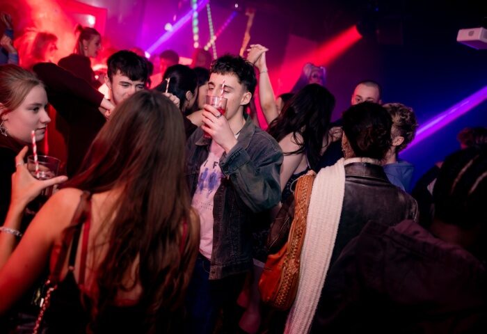 Manchester nightlife: Crowded On Bar scene. People drinking, dancing, and socializing. Red and blue lights illuminate the lively gay bar.