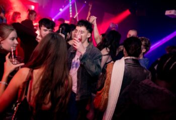 Manchester nightlife: Crowded On Bar scene. People drinking, dancing, and socializing. Red and blue lights illuminate the lively gay bar.