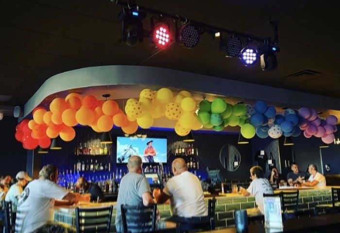 Interior of OneEleven Bar. Rainbow balloons decorate the bar. Patrons sit at the bar, drinks in hand. Gay bar travel.