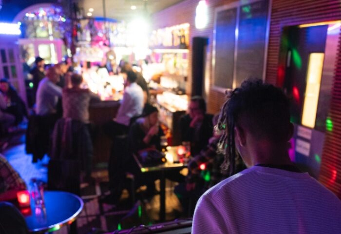 Oscar Bar Cafe Copenhagen scene. Gay bar interior with patrons at bar, tables, and DJ. Nightlife, travel advice.