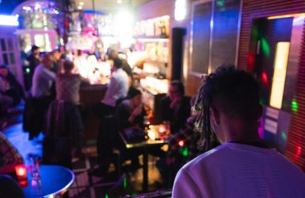 Oscar Bar Cafe Copenhagen scene. Gay bar interior with patrons at bar, tables, and DJ. Nightlife, travel advice.