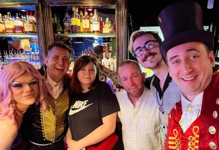 Group at Oscars Bar Manchester, a gay-friendly bar. People smiling, including a drag queen and someone in a top hat.