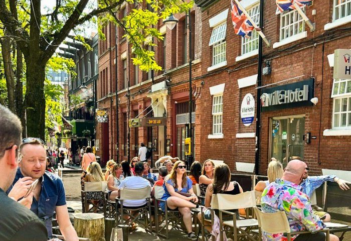 Oscar's Bar in Manchester's Gay Village. People sit outside Ville Hotel, enjoying drinks. A vibrant, welcoming scene for gay travelers.