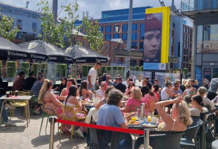 Outdoor seating at Oscars Cafe Bar in Dublin, a gay-friendly spot. People are enjoying drinks and food under Guinness umbrellas. LGBT festival banner.