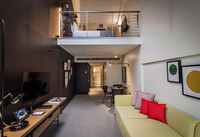 Ovolo Woolloomooloo, Sydney gay hotel room. Loft bed, living area with sofa, TV, and desk. Modern design. Gay travel lodging.