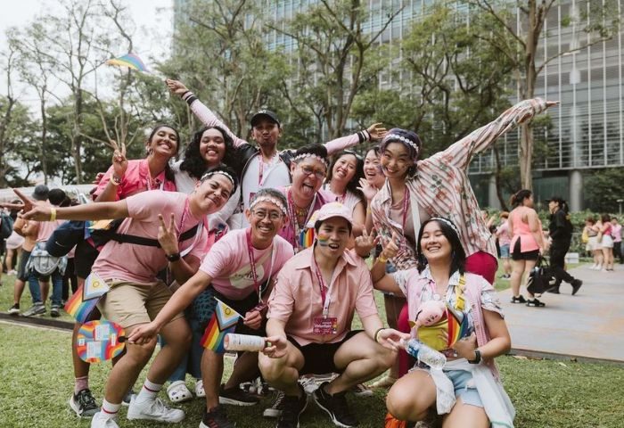 Pink Dot Singapore 2024: Group of smiling people in pink shirts and rainbow accessories at the LGBTQ+ event. Gay travel advice.