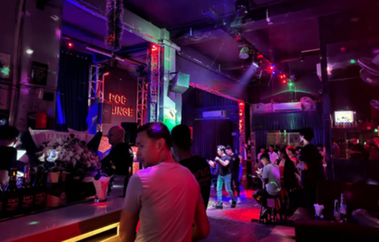 POC Bar, a lively gay bar in Phnom Penh. People are standing at the bar and socializing in the dimly lit, colorful space.