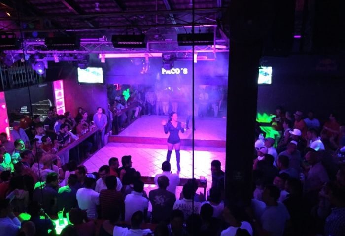 Paco's Ranch gay bar in Puerto Vallarta. A performer on stage with a crowd of people watching, purple lighting, nightlife.