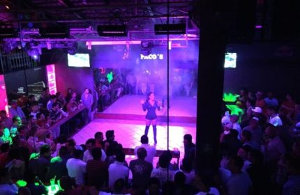 Paco's Ranch gay bar in Puerto Vallarta. A performer on stage with a crowd of people watching, purple lighting, nightlife.