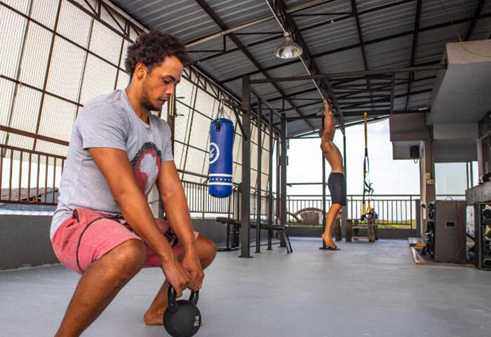Pak Up Hostel Krabi gym: Man doing kettlebell squats, another doing pull-ups. Cheap party gay hotel with fitness for gay travelers.