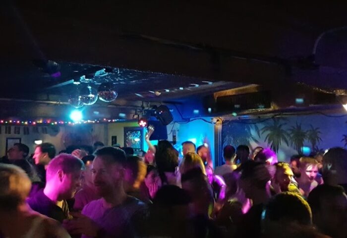 Palms on Oxford, Sydney: Gay men dancing at a crowded gay bar. Disco balls and palm tree mural add to the vibrant atmosphere. Gay travel.