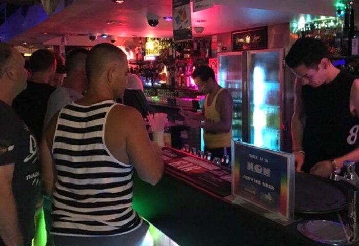 Patrons at Palms on Oxford, a gay bar in Sydney. The bar is busy, with bartenders serving drinks. Gay travel advice.