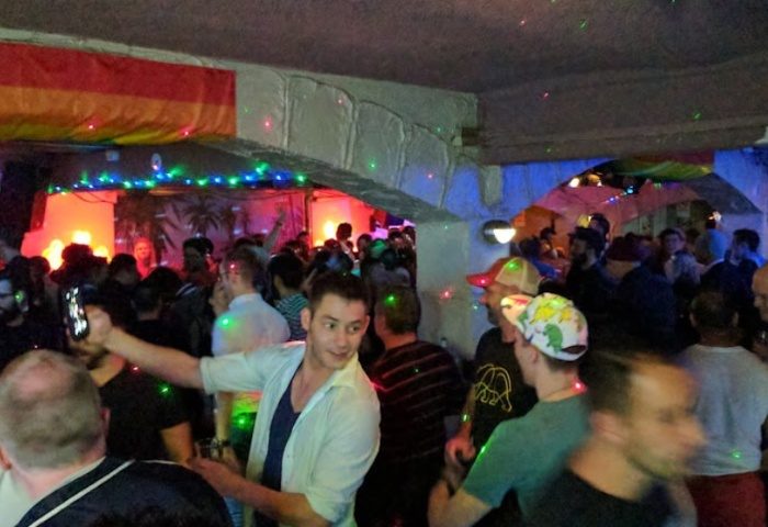 Palms on Oxford, Sydney: Gay men dancing at a crowded gay bar with rainbow flag, colorful lights, and taking selfies. Gay travel advice.