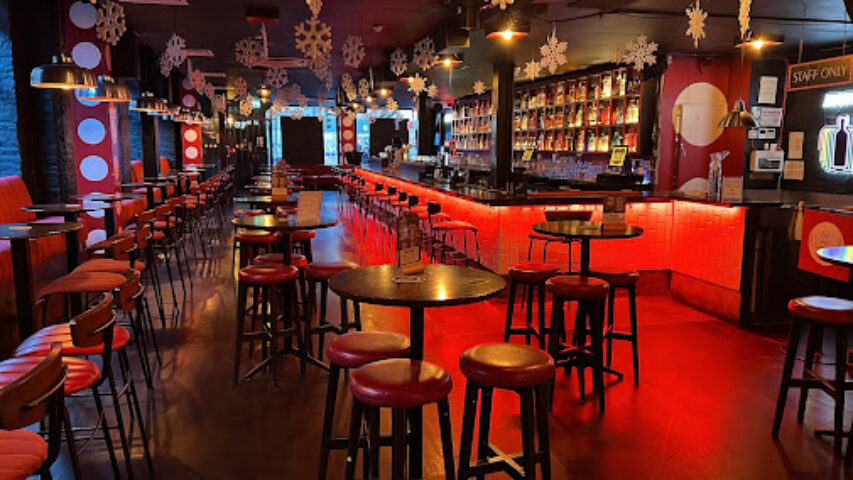 Pantibar gay bar interior in Dublin. Red lighting, stools, tables, and a fully stocked bar. A popular spot for gay men's travel.