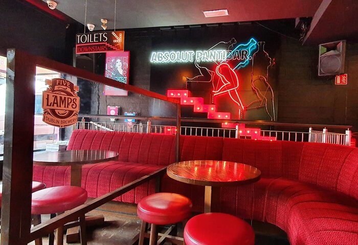 Pantibar Gay Bar, Dublin interior. Red seating, tables, and stools. Neon sign Absolut Pantibar. Toilets downstairs sign. Gay travel advice.