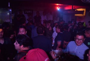Crowded Papi Fun Bar gay party scene in Mexico. Men socializing, drinking, and enjoying the nightlife in a dimly lit club. Gay travel.