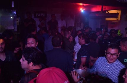 Crowded Papi Fun Bar gay party scene in Mexico. Men socializing, drinking, and enjoying the nightlife in a dimly lit club. Gay travel.