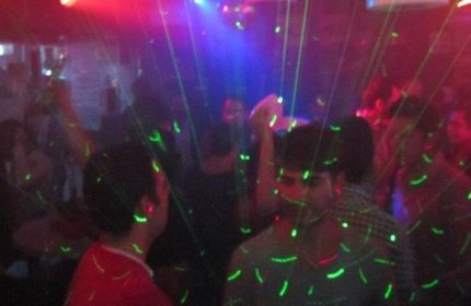 Gay party at Papi Fun Bar in Mexico. Crowd of men dancing under laser lights. Nightlife scene, travel destination.