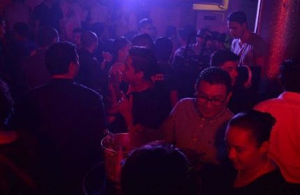 Crowded Papi Fun Bar gay party in Mexico. People socializing under blue and red lights. Gay travel advice, nightlife scene.