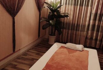 Paradise Spa, Ho Chi Minh: Massage bed with orange towel, white pillow, potted plant, and decorative curtains. Gay travel relaxation.