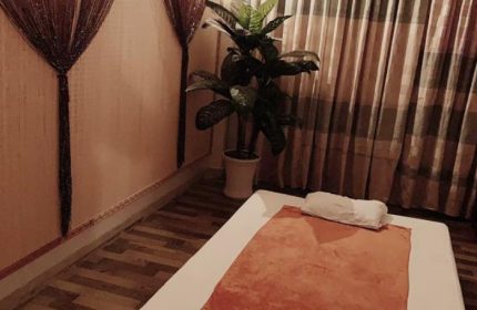 Paradise Spa, Ho Chi Minh: Massage bed with orange towel, white pillow, potted plant, and decorative curtains. Gay travel relaxation.