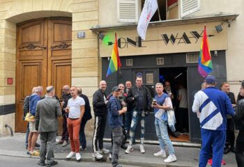 Paris One Way: Gay men gather outside a bar with rainbow flags. Travel advice for gay tourists in Paris, France.
