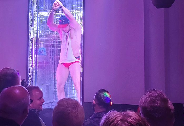 Paris RAIDD Bar: Go-go dancer in red briefs performs on stage. Gay nightlife scene in Paris. Audience members watch the show at RAIDD.